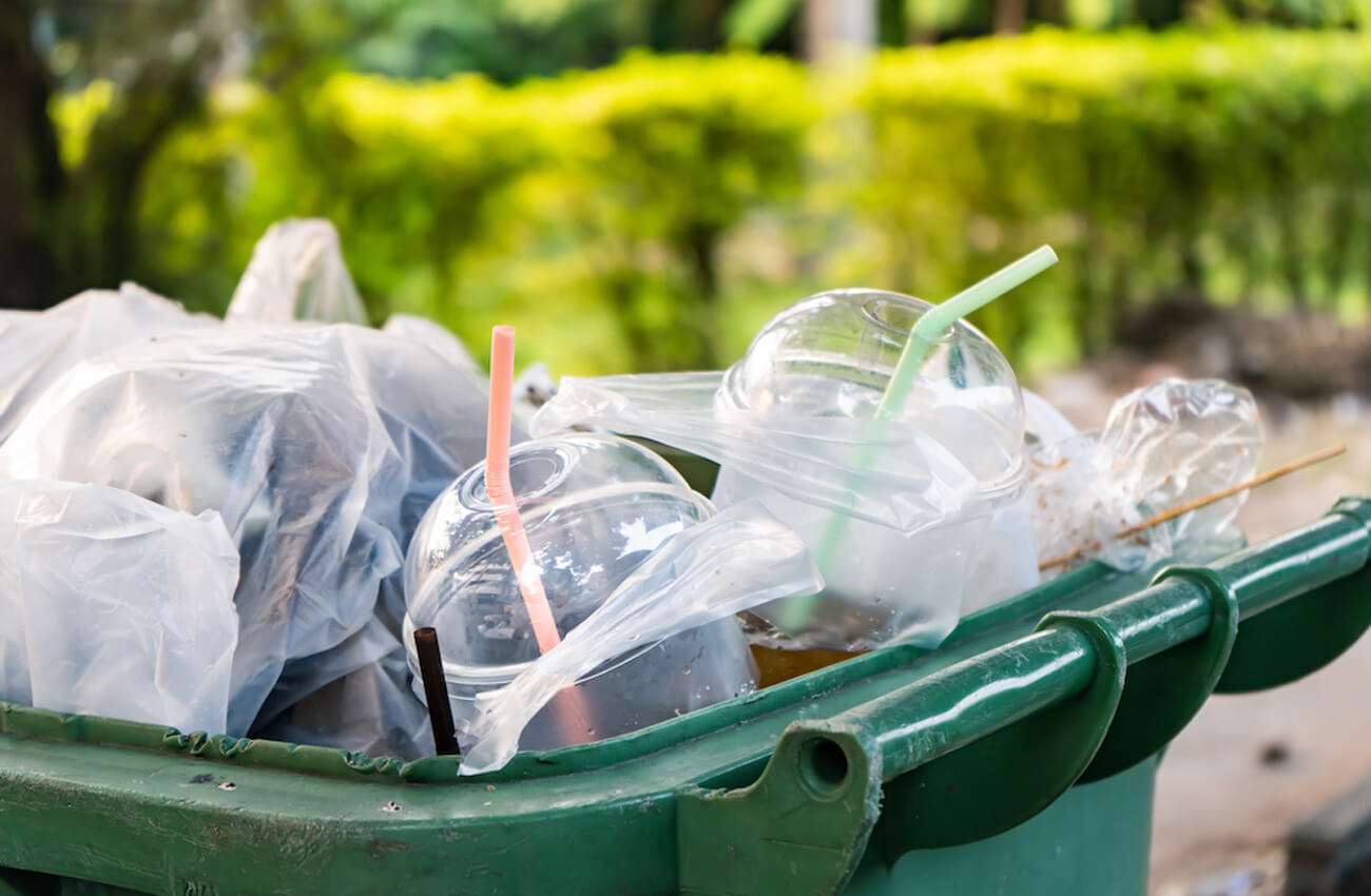 A recycling bin filled single used plastics — namely, plastic cups with straws.